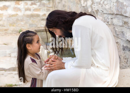 Scena biblica quando Gesù dice, lasciate che i bambini vengano a me, la benedizione di una bambina. La rievocazione storica di un antico pozzo di acqua. Foto Stock