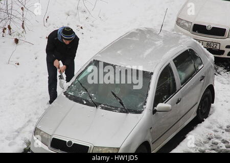 Il proprietario di un'autovettura in Praga area Libeň raschia fuori la neve e il gelo sul suo veicolo al fine di essere in grado di estrarre la sua auto parcheggiata. Foto Stock