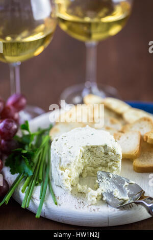 Soft aromatizzato il formaggio cremoso con aglio ed erbe fini su un pannello di legno con cracker. Foto Stock