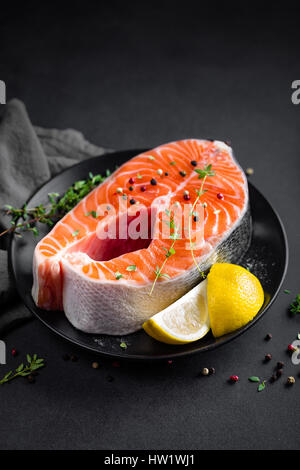 Pesce salmone bistecca con limone e timo su sfondo nero Foto Stock