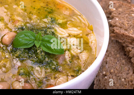 Fresche minestrone, fatta con verdure miste, bianco cannelini fagioli e pasta conchiglie, guarnita con un fresco e pesto di basilico, olio e un rametto di bas fresco Foto Stock