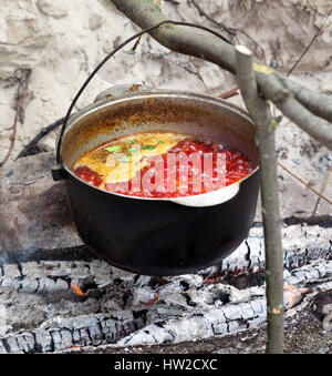 Borscht (Ucraino zuppa tradizionale) cottura nel calderone di fuliggine sul fuoco. Messa a fuoco selettiva sul pot. Foto Stock