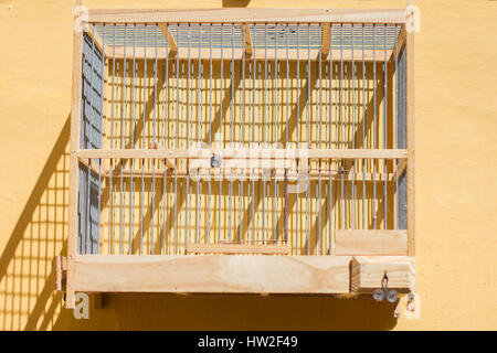 Vuoto birdcage di legno appeso alla parete gialla Foto Stock