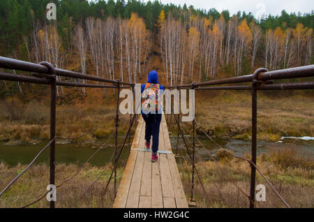 La donna caucasica Varcando il fiume sulla passerella in legno Foto Stock