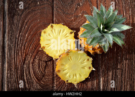 Fresh Asian ananas piccola sul piatto di legno in outdoor il disco alla luce diretta del sole e ombra scura Foto Stock