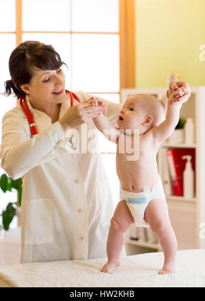 Felice simpatico baby a salute esame presso l'ufficio del medico. Pediatra supporta il neonato bambino mentre si sta in piedi Foto Stock