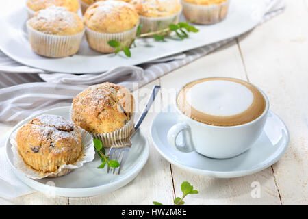 Pane appena sfornato cioccolato muffin alla banana con glassa di zucchero servito con una tazza di cappuccino Foto Stock
