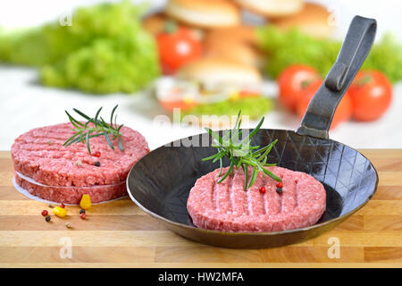 Materie burger Patty in un ferro da stiro padella pronto per friggere, alcuni ingredienti burger in background Foto Stock