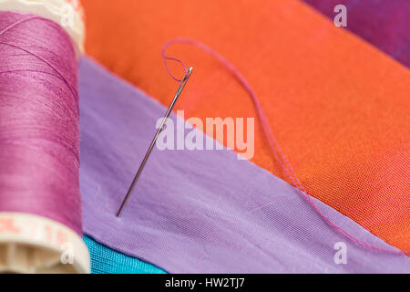 Filo passante per ago close-up su sfondo arancione. La bobina di violetta filettature sul tessuto colorato, macro. produzione di mosaico, fatta a mano. Foto Stock