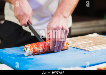 Tagliare la cipolla a pezzi. Tappetino di piccole dimensioni sul bordo di cottura. Lo chef giapponese al lavoro. L uomo si prepara sushi rotoli. Foto Stock