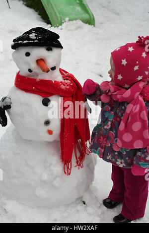 I bambini che giocano sulla neve, Dublino, Irlanda toddler bambina, snowman gioia divertimento, carota naso, sciarpa rossa, infanzia felice, divertimento invernale Foto Stock