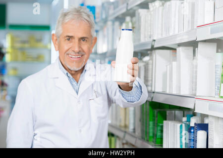 Ritratto di sorridente farmacista maschio tenendo bottiglia di shampoo in farmacia Foto Stock