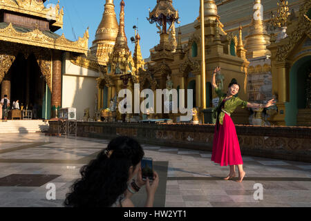 Una donna pone in una danza mentre ella è girato su un telefono mobile in corrispondenza della Shwedagon pagoda in Yangon, Regione di Yangon, Myanmar Foto Stock