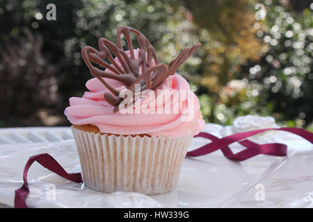 Un fresco, organico reso Glassa alla fragola, vaniglia tortina in tenui colori rosa con un sentore di viola e una deliziosa decorazione chocolatebutterfly sul ghiaccio Foto Stock