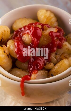 Foto verticale con due ciotole impilati piena di gnocchi fatti in casa. Porzione di pasta viene collocato su vintage tagliere in legno con superficie usurata. Rosso ketchup sauc Foto Stock