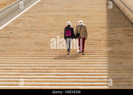 Due vecchie persone che camminano mano nella mano insieme i gradini di pietra di Renzo Piano progettato di entrata e il palazzo del parlamento presso la città di La Valletta Foto Stock