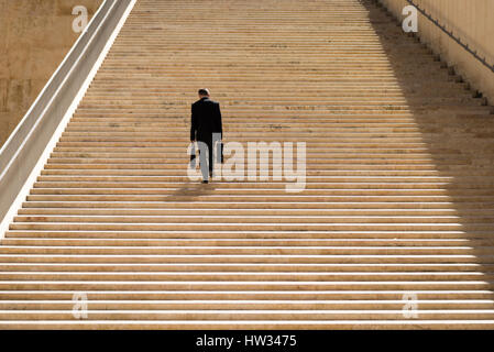 Un imprenditore in un vestito che porta due valigette a piedi fino alla scalinata in pietra dal Parlamento edificio progettato da Renzo Piano nella valletta di Malta Foto Stock
