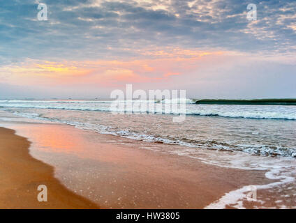 India, Goa. La mattina presto sulla spiaggia Colva. Rising Sun si illumina le nuvole. Foto Stock