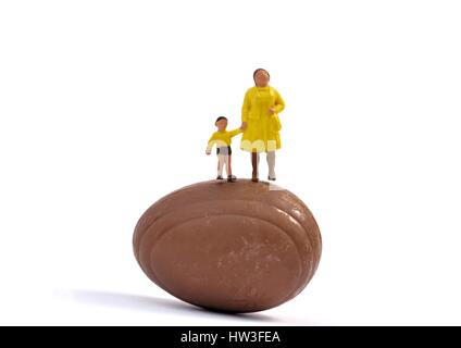 Statuetta in miniatura, donna e bambino in piedi sulla sommità di un piccolo uovo di cioccolato Foto Stock