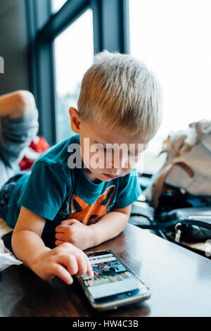 Razza mista boy posa sulla tabella utilizzando il telefono cellulare Foto Stock