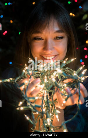 Razza mista donna che mantiene le luci della stringa nei pressi di albero di Natale Foto Stock
