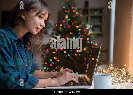 Razza mista donna utilizzando laptop vicino albero di Natale Foto Stock