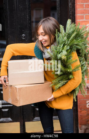 Razza mista donna portante ghirlanda di pino e scatole di cartone Foto Stock