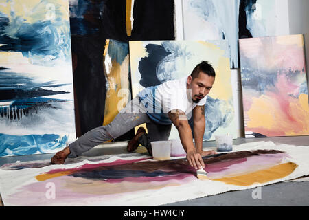 Pacific Islander artista inginocchiati sul pavimento dipinto su tela Foto Stock
