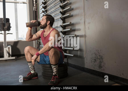 Razza mista uomo di bere dalla bottiglia in palestra Foto Stock