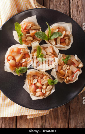 Tazze di pasta filo farcito con mele e arachidi close-up su una piastra. Vista verticale da sopra Foto Stock