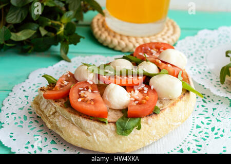 Classico panino con mozzarella, pomodoro fresco, rucola e semi di sesamo sul pane tostato. La prima colazione. Foto Stock