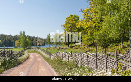 Il pittoresco paese strada che conduce a un lago attraverso un bellissimo paesaggio rurale, Smaland, Svezia e Scandinavia. Foto Stock