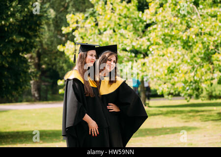 Riga, Lettonia - 1 Luglio 2016: due giovani donne laureati dell'Università di Lettonia vestito in abito di laureati e piazza cappucci accademico che posano per una foto Foto Stock