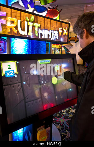 L'uomo scorri le dita sullo schermo durante la riproduzione di Fruit Ninja FX gioco in un video arcade a Long Beach, Washington. Foto Stock