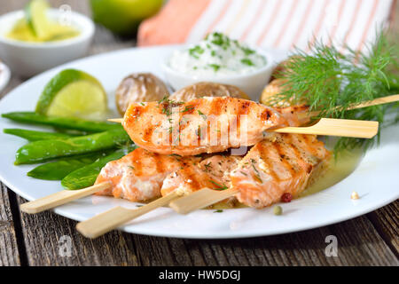 Salmone alla griglia serviti spiedini con la neve di piselli e patate al forno con panna acida Foto Stock