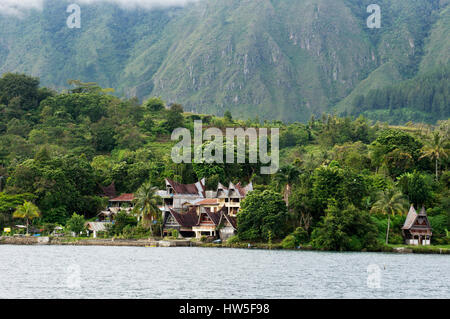 Numerose case costruire ai piedi di una montagna vicino al lago di ta in Sumatra isola di Samosir nel pomeriggio, Indonesia. Foto Stock