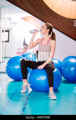 Giovane donna seduta su sfere di pilates , appoggiato dalla formazione e acqua potabile Foto Stock