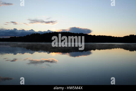 Prima dell'alba sul lago in campagna polacca - cielo nuvoloso e silhouette di foresta Foto Stock