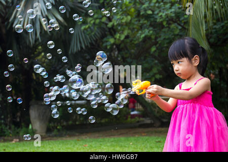 Asian poco ragazze cinesi bolle riprese dal ventilatore di bolla nel Parco Foto Stock
