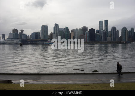 Uomo a piedi attraverso il Parco Stanley con la città di Vancouver in background. Foto Stock