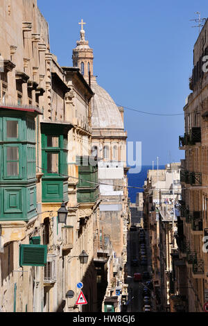 Verticale di street view a La Valletta, Malta, passato balconi Ottomano con Anglicana di San Paolo pro-cattedrale, cielo blu e blu del mare in lontananza Foto Stock