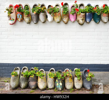 Tradizionale artigianale olandese scarpe di legno su un muro di mattoni pieni di fiori. Foto Stock