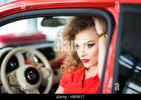 La bellezza della donna nella piccola auto rossa in posa Foto Stock