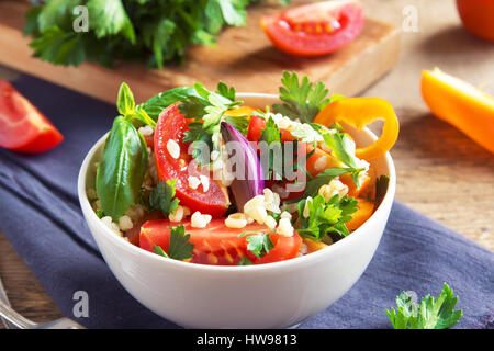 Organico fresco di pomodoro e cuscus insalata di bulgur tabulé con verdure e verdi - vegetariana sana dieta vegana insalata tradizionale in legno rustico Foto Stock