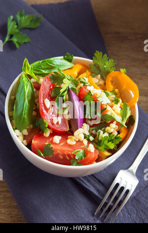 Organico fresco di pomodoro e cuscus insalata di bulgur tabulé con verdure e verdi - vegetariana sana dieta vegana insalata tradizionale in legno rustico Foto Stock