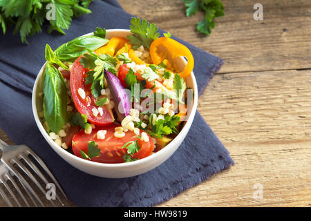 Organico fresco di pomodoro e cuscus insalata di bulgur tabulé con verdure e verdi - vegetariana sana dieta vegana insalata tradizionale in legno rustico Foto Stock