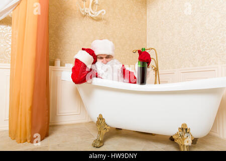 Funny ubriaco Babbo Natale con bottiglia di alcool in mano dormire in una vasca da bagno. Natale umorismo Foto Stock