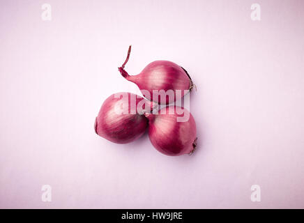 Tre cipolle rosse su sfondo viola, vista dall'alto Foto Stock