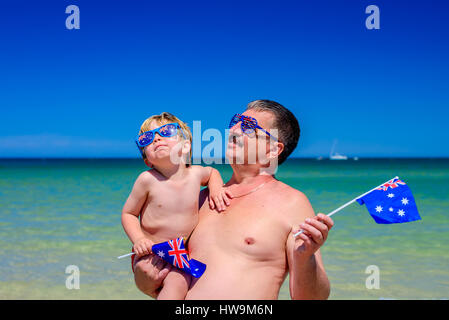 Carino il ragazzo sorridente con il suo nonno e bandiere australiano in piedi sulla spiaggia il giorno in Australia Foto Stock