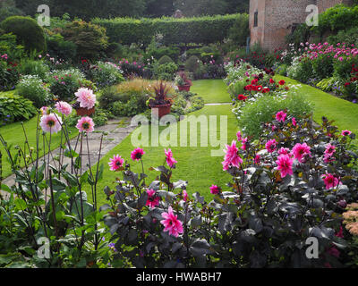 Chenies Manor giardino, Buckinghamshire. Il sunken giardino Dahlia display in piena fioritura. Vista del paesaggio, vivid i confini di piante e prato verso il padiglione. Foto Stock